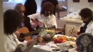 From left to right, George Harrison, Tom Petty, Jeff Lynne, and Bob Dylan all sitting around a table playing guitars in George Harrison: Living In The Material World