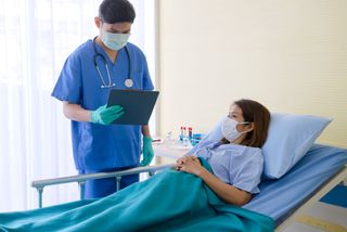 Doctor and patient in hospital room wearing masks.