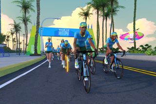 A screengrab of Zwift riders on a paved road with a Tour of Watopia blue arch behind them.