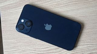 En blå iPhone 13 Mini ligger på ett ljust träfärgat bord med baksidan vänd uppåt.