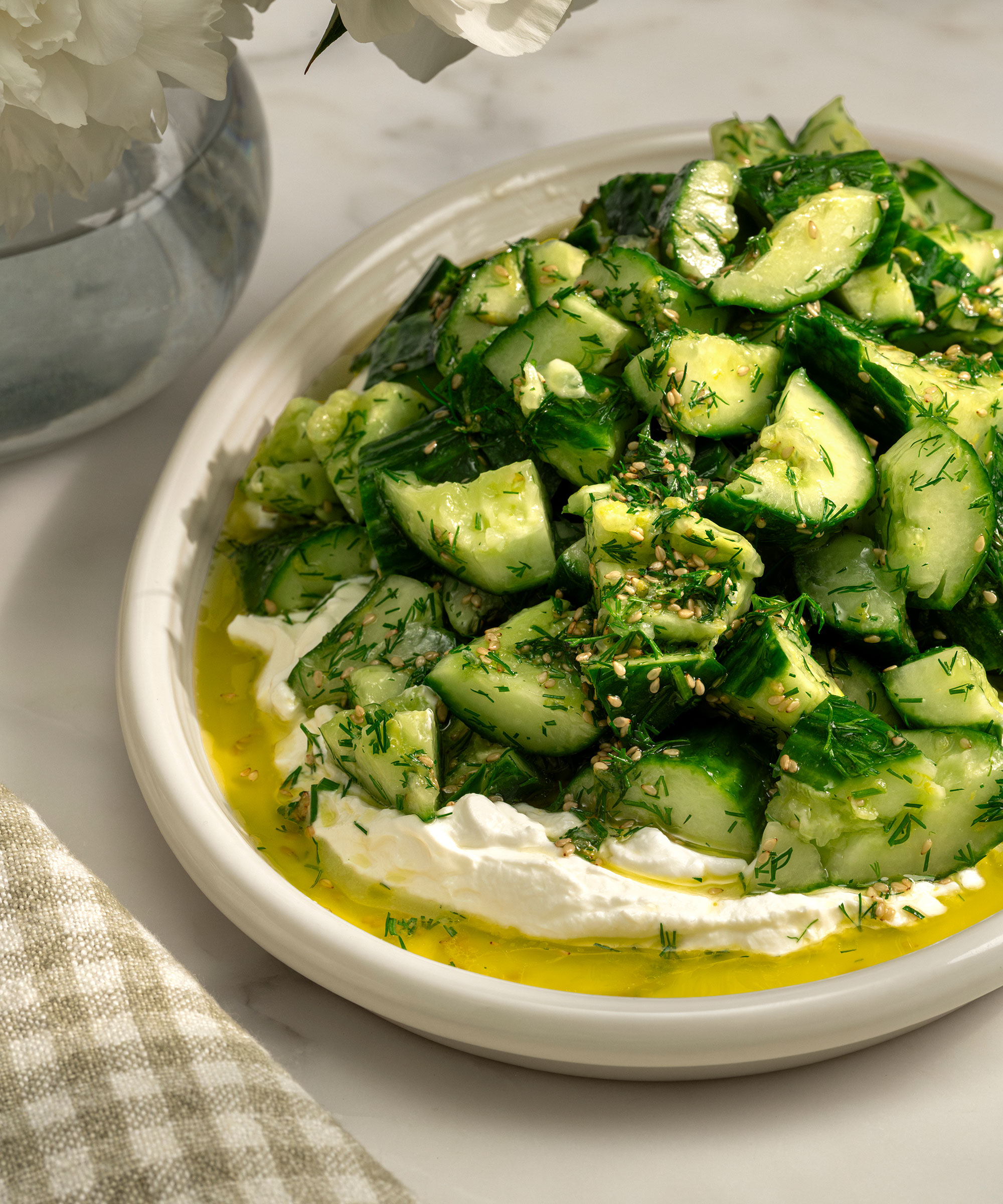 A high-angle, close-up photograph of a vibrant Tzatziki Cucumber salad, featured in Shea McGee&amp;rsquo;s cookbook, Around the Table