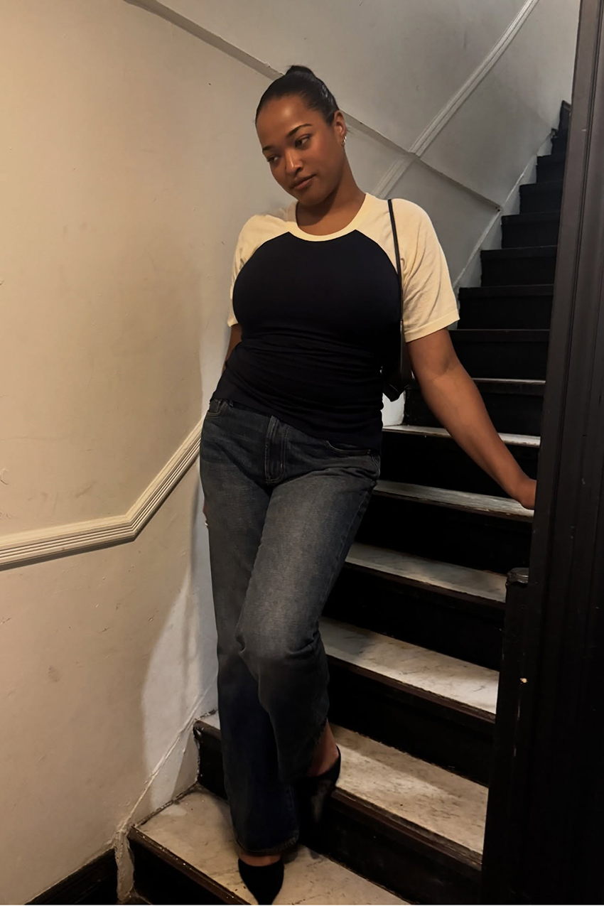 a woman wearing a white and black shirt, dark wash jeans, and pointed-toe shoes