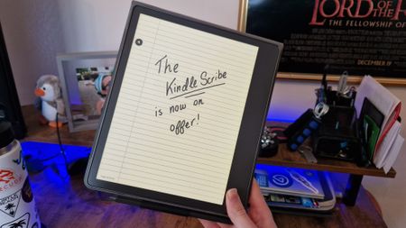 A Kindle Scribe being held, on it screen someone has writen "the kindle scribe is now on offer"