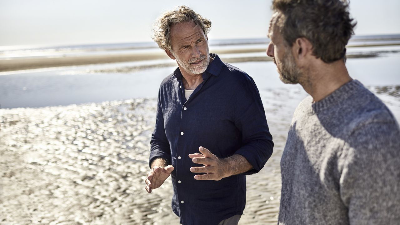 A father and son walk on the beach while having a serious discussion.