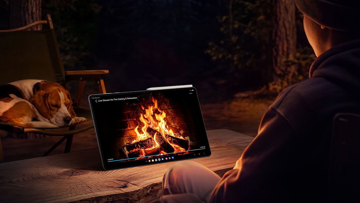 A man using a Samsung Galaxy Tab S12 Ultra at home watching a fireplace