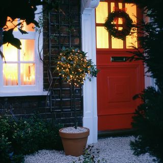 House exterior with red front door wreath and bay tree with fairy lights