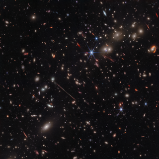 A full-size version of the new JWST El Gordo image. Various distorted galaxies are seen against the backdrop of space.
