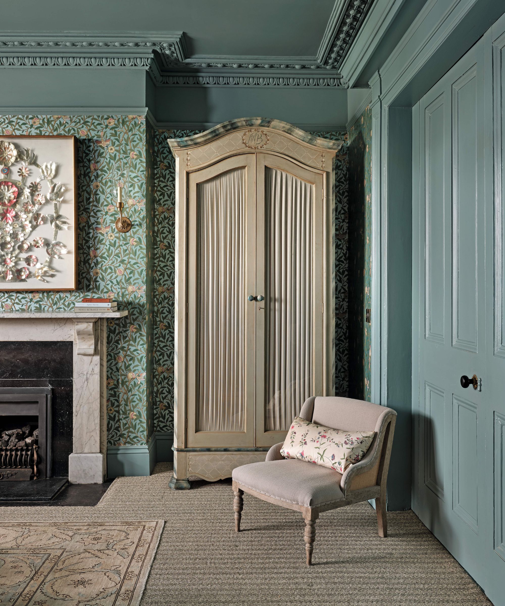 a blue color drenched bedroom with floral wallpaper, marble fireplace and an antique wardrobe