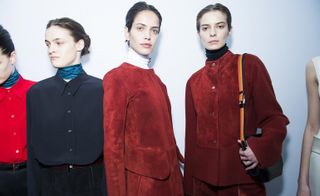 Four female models, one in a red shirt with blue scarf, one in a navy shirt with blue scarf and two in red suede outfits