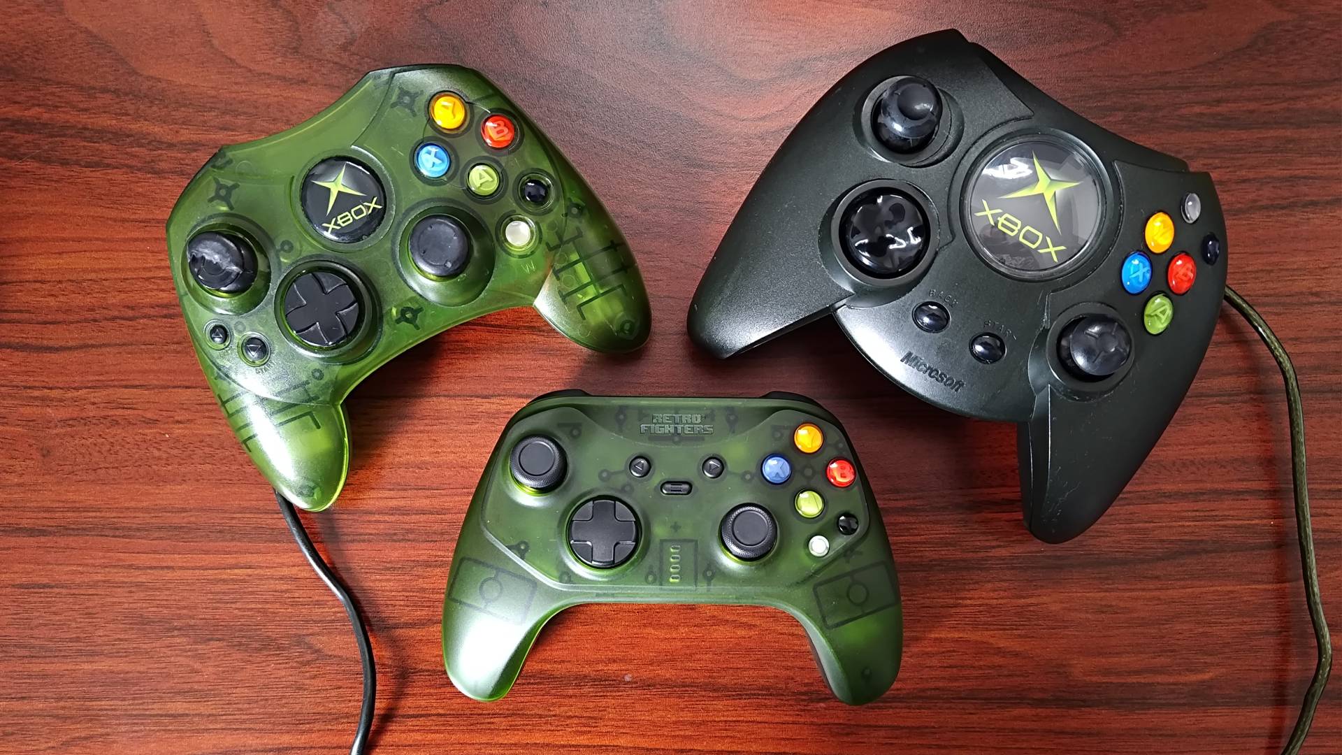Retro Fighters Hunter with OG Xbox S controller on top left and Duke on top right with all three sitting on woodgrain desk.