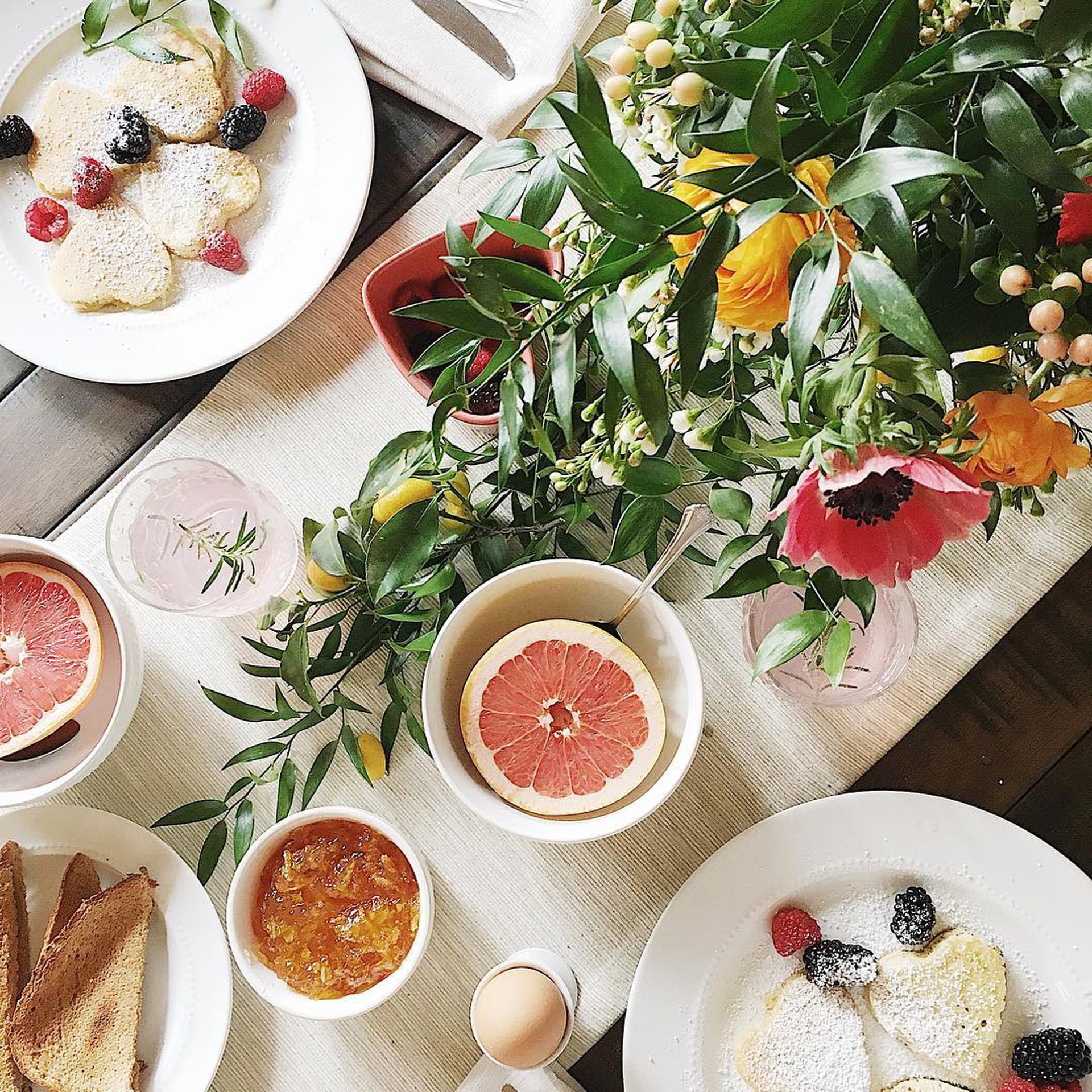 Pemandangan meja makan siang yang segar dan berwarna-warni dengan belahan grapefruit, dedaunan hijau, dan bunga pop berwarna-warni