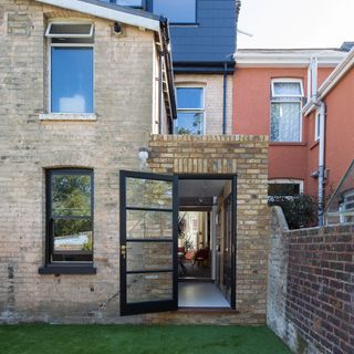 a view of the exterior of a two storey brick house, showing the glass with black frame back door open