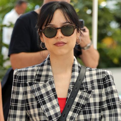 Jenna Ortega wearing a plaid blazer, a red top, and sunglasses 