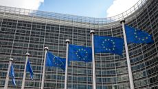 Facade of the Berlaymont building, headquarters of the European Commission, in Brussels, with EU flags fluttering in the wind.