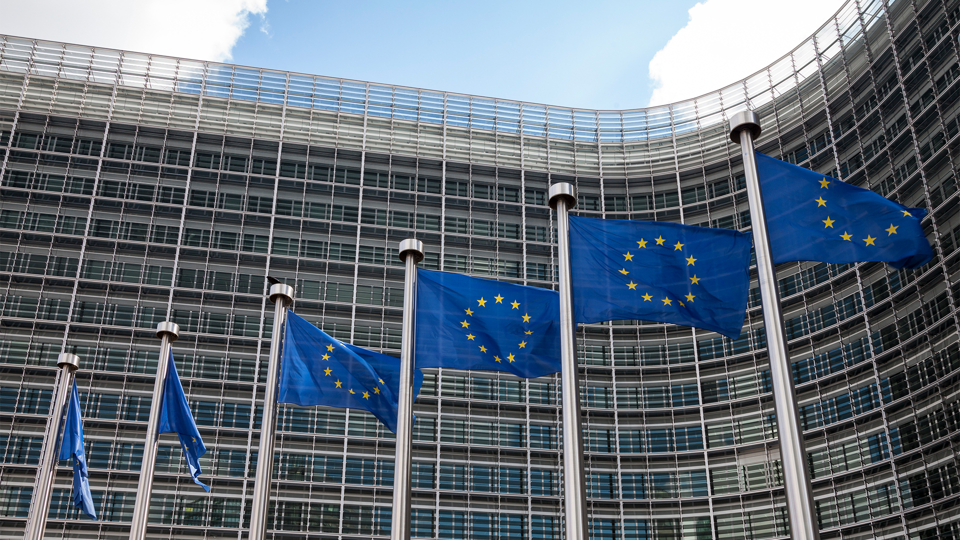 Facade of the Berlaymont building, headquarters of the European Commission, in Brussels, with EU flags fluttering in the wind.
