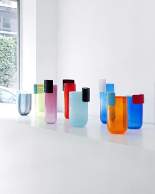 Colourful cynlinder glass vases in different sizes and heights placed on a white surface against a white wall with a peek of a window on the left