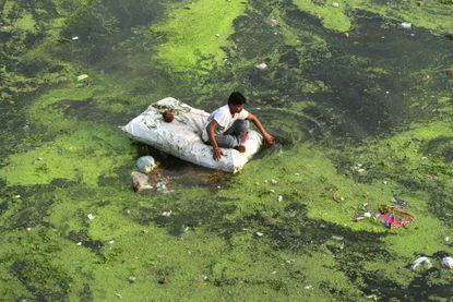 An Indian man sits on a raft in a polluted river