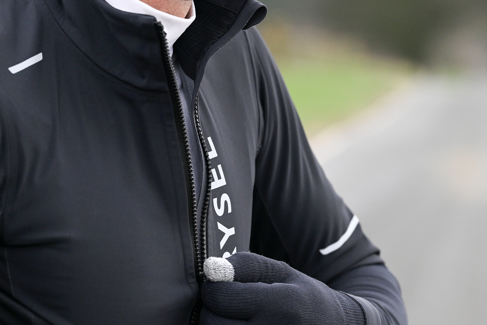 Close up of a man zipping up a black jacket whilst wearing gloves