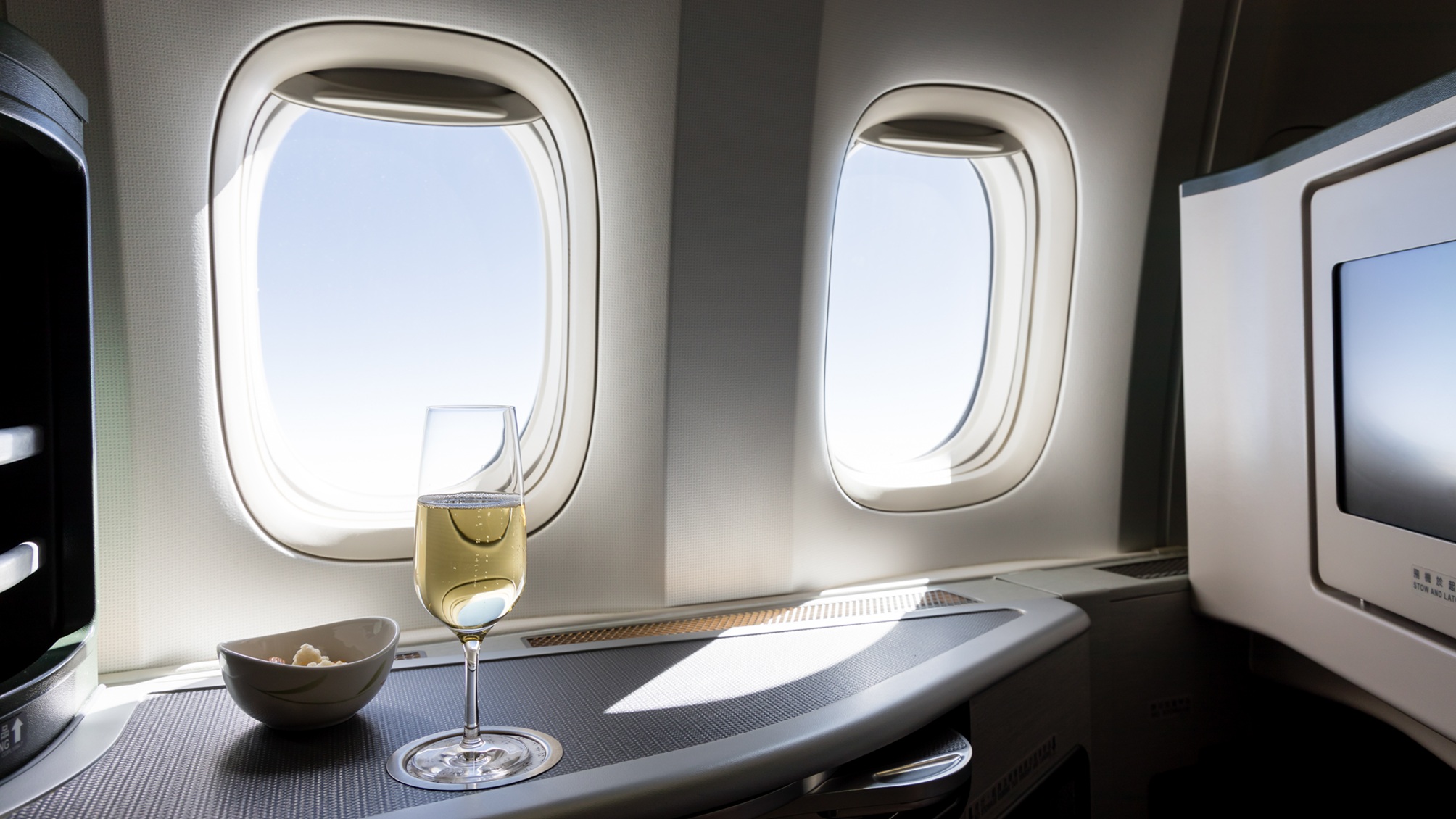 A glass of wine and a small bowl of snacks on a table in business or first class of an airplane.