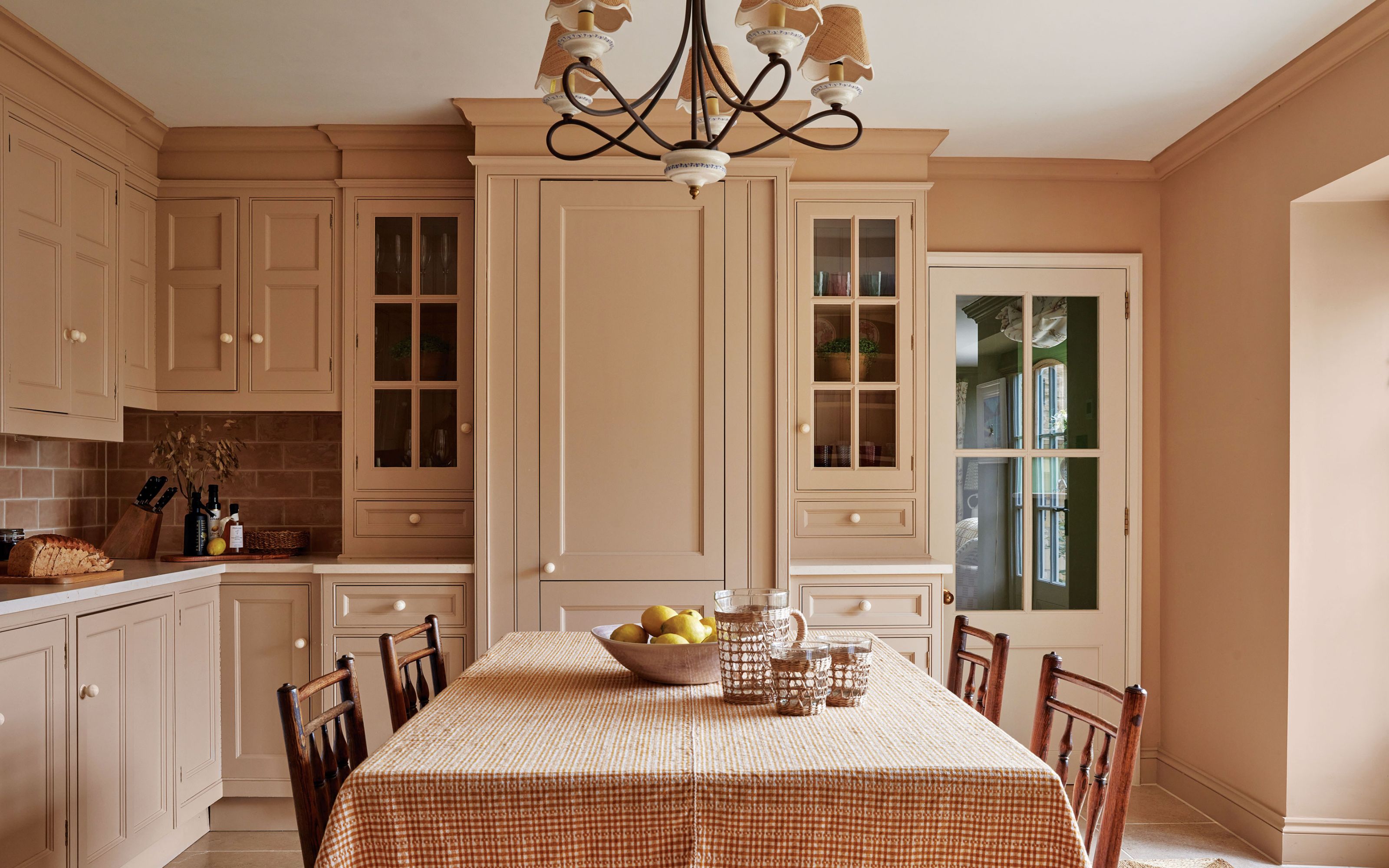 Kitchen with pink cabinetry and walls, table with cloth over plus wooden chairs