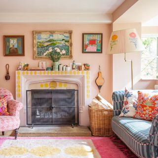 cottagecore decor ideas for living rooms, colourful living room with decorated fireplace, pastel pink walls, rugs, blue print sofa, bright cushions, Charleston style prints, mix and match patterns