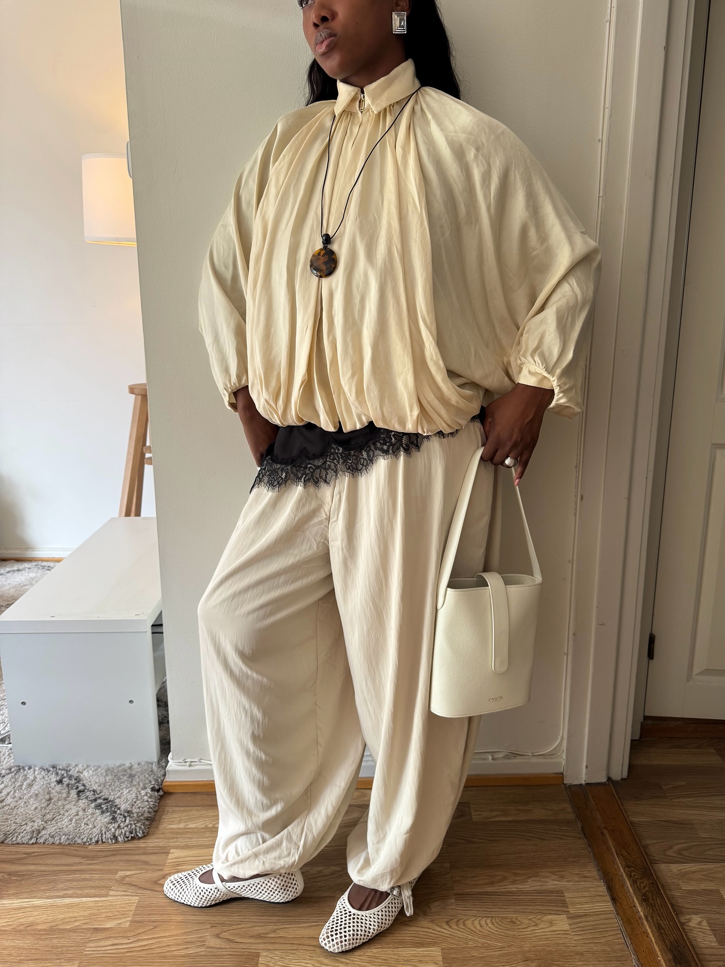 An image of @nnennaechem wearing a pair of cream balloon pants with a windbreaker, pendant necklace and lace-trim top.