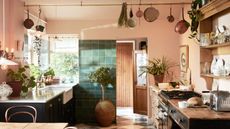 A salmon pink kitchen with a rail and copper pans hanging from it as well as a view of the kitchen counters with kitchen essentials on top