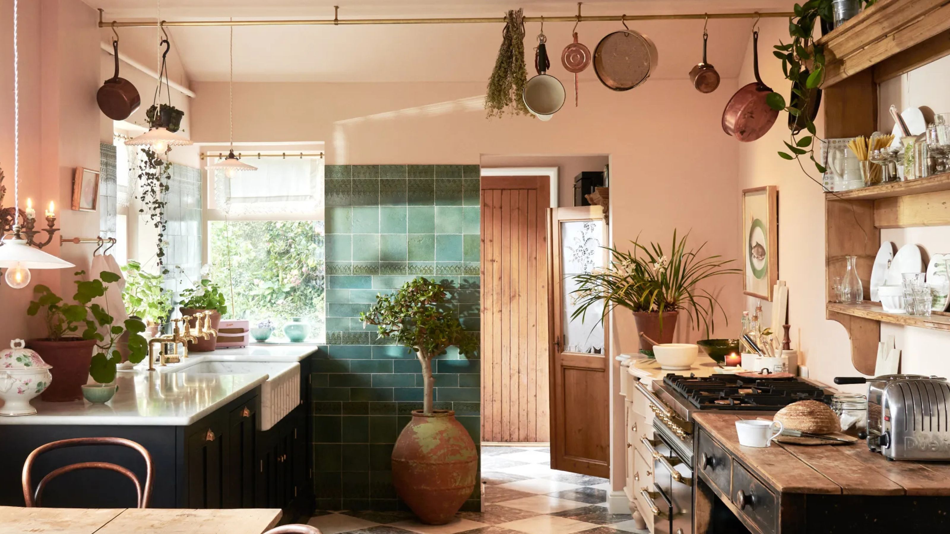 A salmon pink kitchen with a rail and copper pans hanging from it as well as a view of the kitchen counters with kitchen essentials on top 