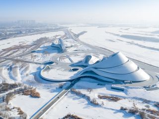 Harbin Opera House is a very modern construction that looks like a bent paper shape. The photo is taken in the winter and the snow covers the surroundings.