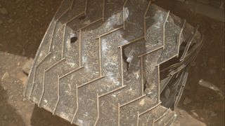 A photo of one of the Curiosity rover's wheels with several tears in its scratched surface