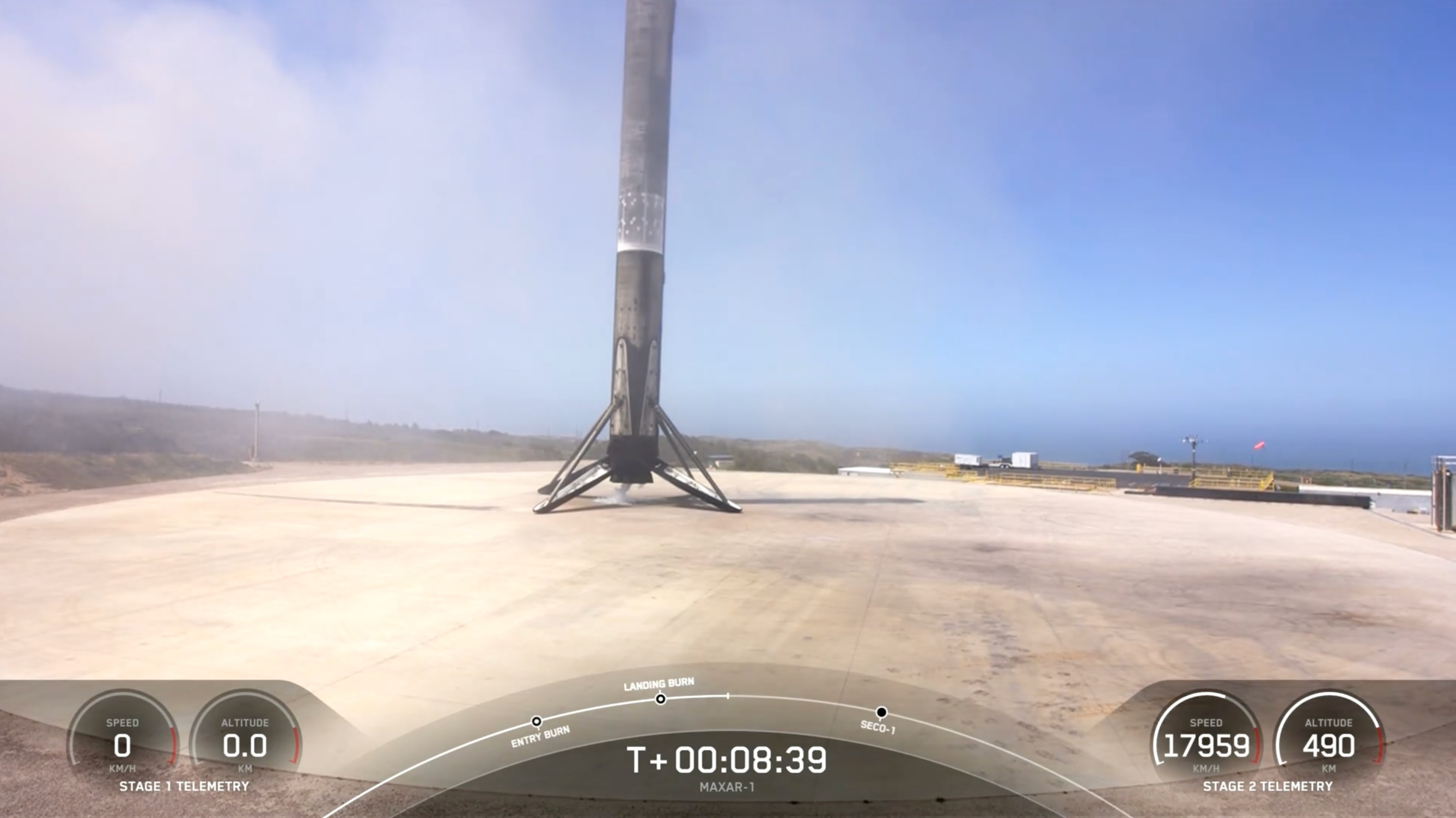 The first stage of a black-and-white SpaceX Falcon 9 rocket is placed on the landing pad shortly after landing.