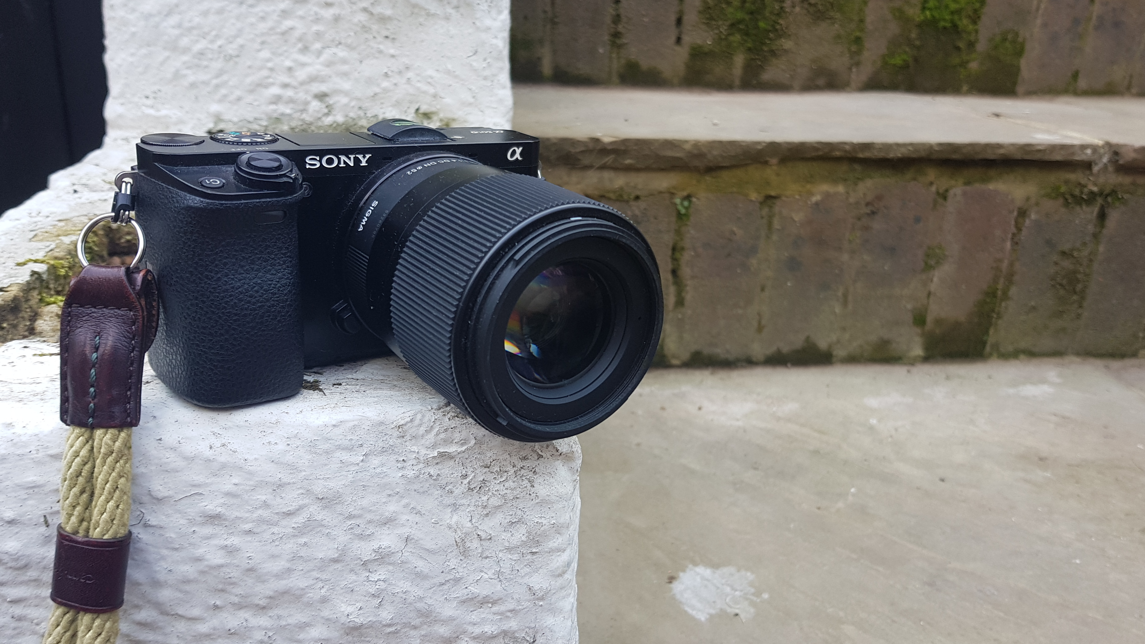 Photograph of Sony A6000 camera on stone wall with 30mm lens and wrist strap