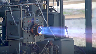 A pointy nozzle on a test stand spits diamonds of fire.