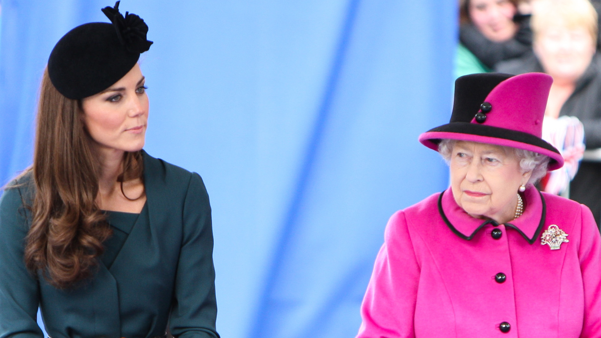 Kate Middleton wears a dark green dress with a black hat and Queen Elizabeth wears a bright pink coat