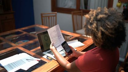 A person sitting at a desk photographing documents to safeguard financial documents.