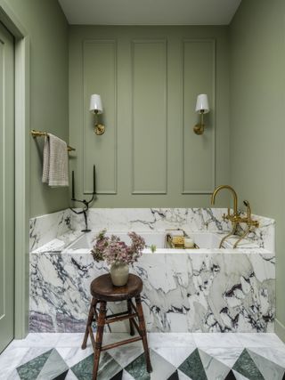 A bathroom drenched in sage green with a marble bathtub