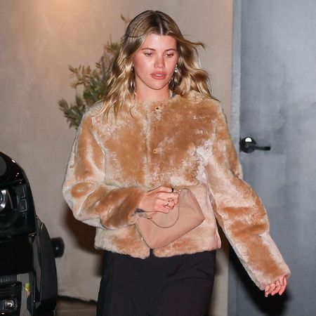 Sofia Richie steps out wearing a faux fur jacket with black trousers and black kitten heel flip-flops. She carries a beige bag in her hands.