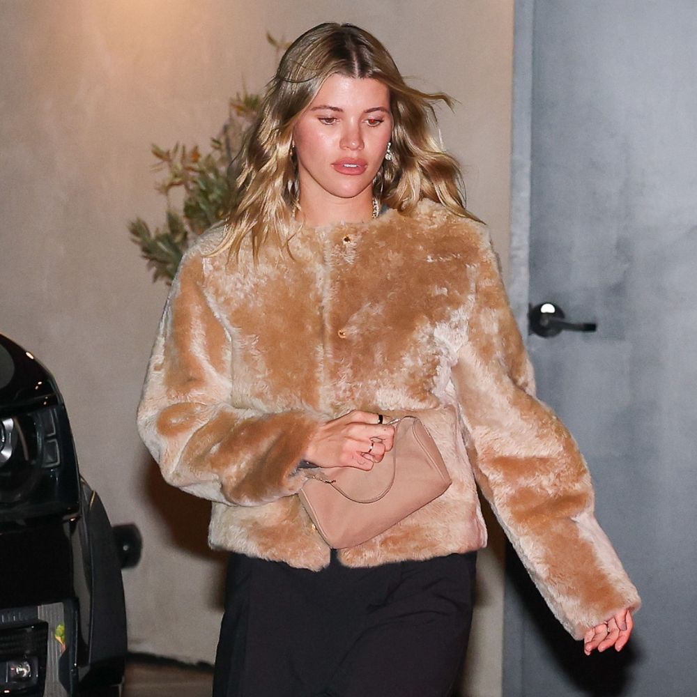 Sofia Richie steps out wearing a faux fur jacket with black trousers and black kitten heel flip-flops. She carries a beige bag in her hands.