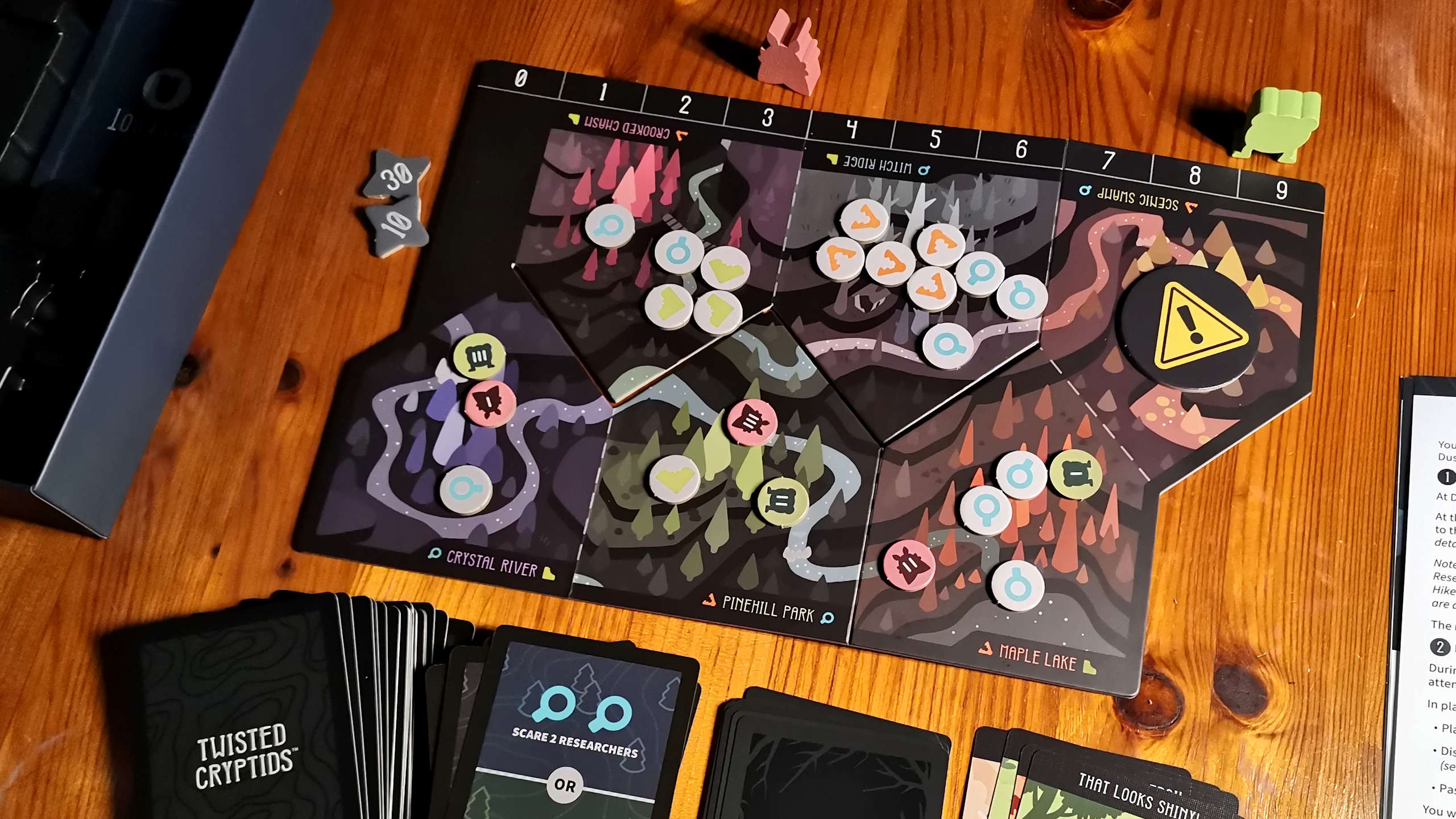 Twisted Cryptids board pieces and tokens on a wooden surface