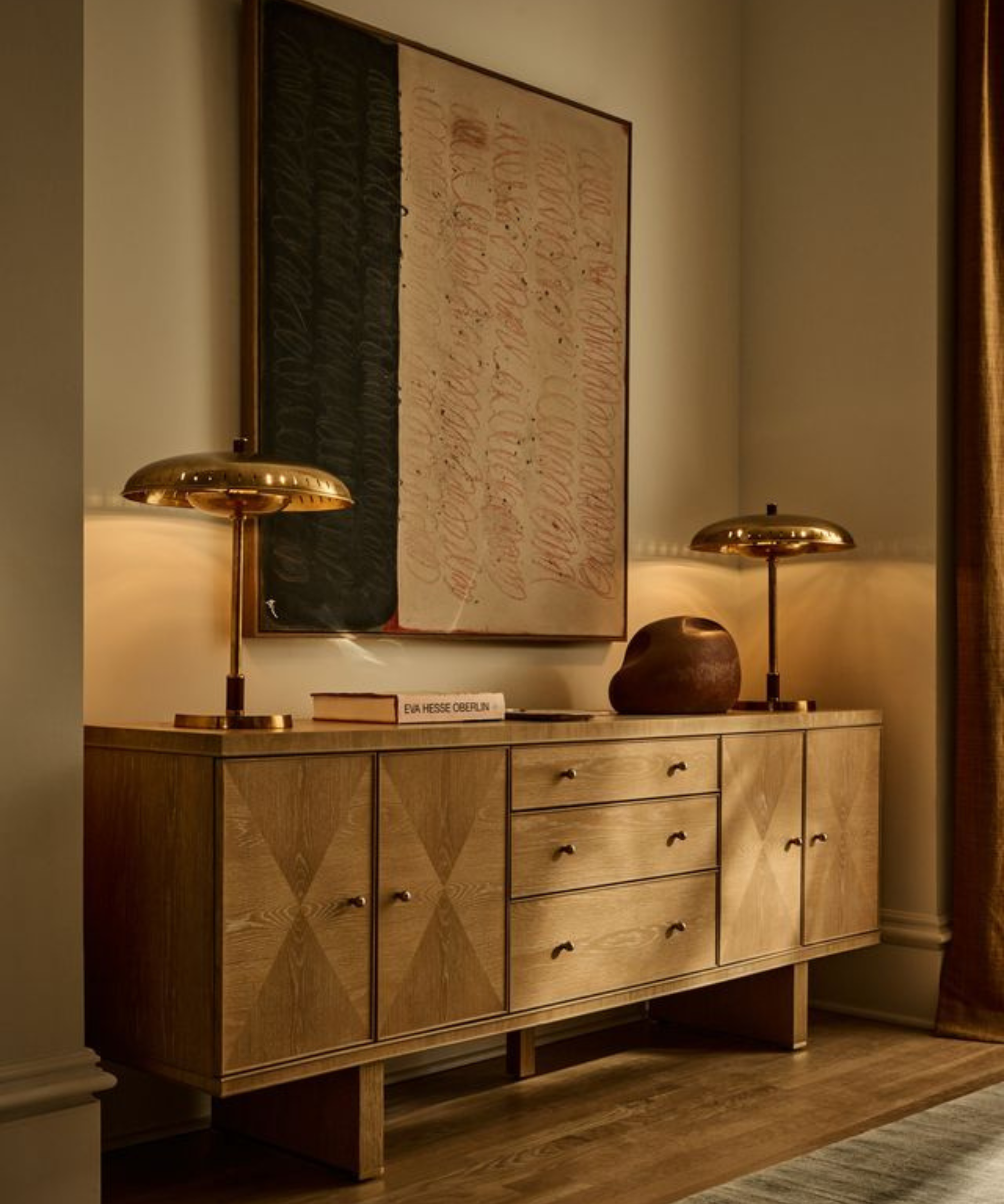 a credenza with several shelves and doors, two brass lamps on top, and a painting hanging from the wall