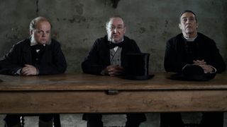 Dr. McBrearty (Toby Jones), Sir Otway (Dermot Crowley) and Father Thaddeus (Ciaran Hinds) sitting together at a long table in The Wonder