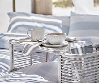 hampton coffee mug with a bowl on a mini table outside on blue and white bedding