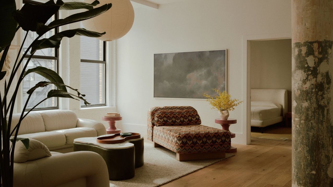 modern loft-style living room with timber floors, beige rug, beige corner sofa, patterned chaise lounge, round coffee table, artwork on wall, and paper lantern hanging overhead