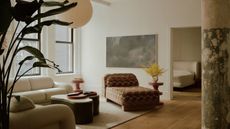 modern loft-style living room with timber floors, beige rug, beige corner sofa, patterned chaise lounge, round coffee table, artwork on wall, and paper lantern hanging overhead