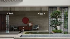 A home in Tirupur, India with a beautiful porch featuring a koi pond, a bonsai tree, a pair of gray armchairs, a vase with bird of paradise, a red wall hanging, and a peacock statue