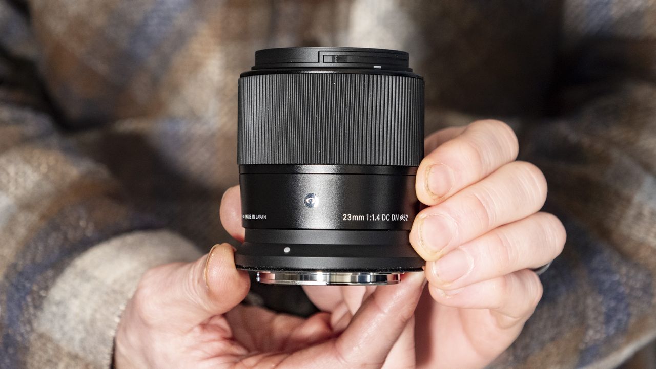 Sigma 23mm F1.4 DC DN Contemporary lens in the hand, checked shirt background