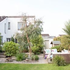 View from the lawn towards the gravelled and decked patio area with garden seating and trees. 