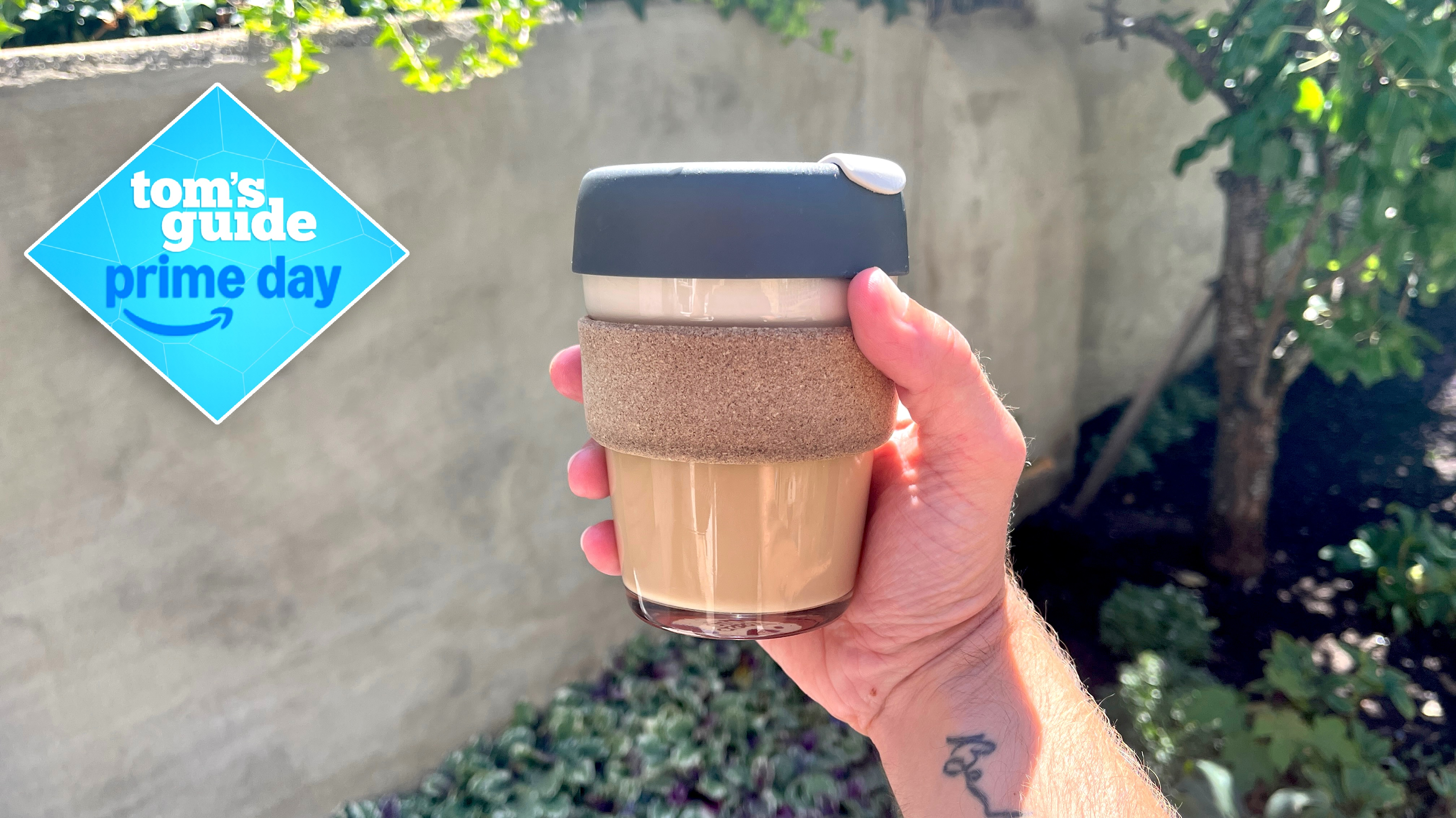 Person holding the KeepCup 12oz Reusable Coffee Cup outside in front of a wall with plants in the background