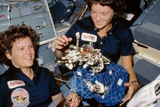two women astronauts in space shuttle holding hardware
