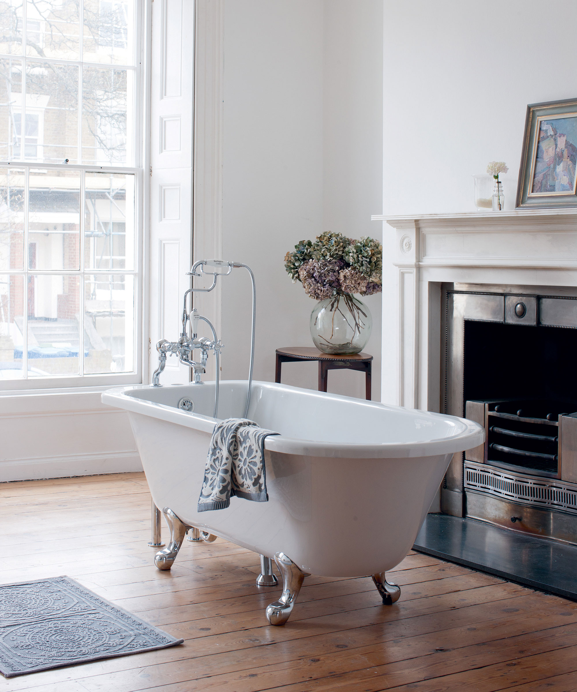 traditional bathroom with freestanding rolltop bat and original fireplace in room with sash windows